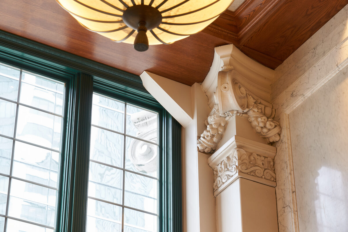 Ornate Corinthian capital atop a marble column with period ceiling light and green window frames