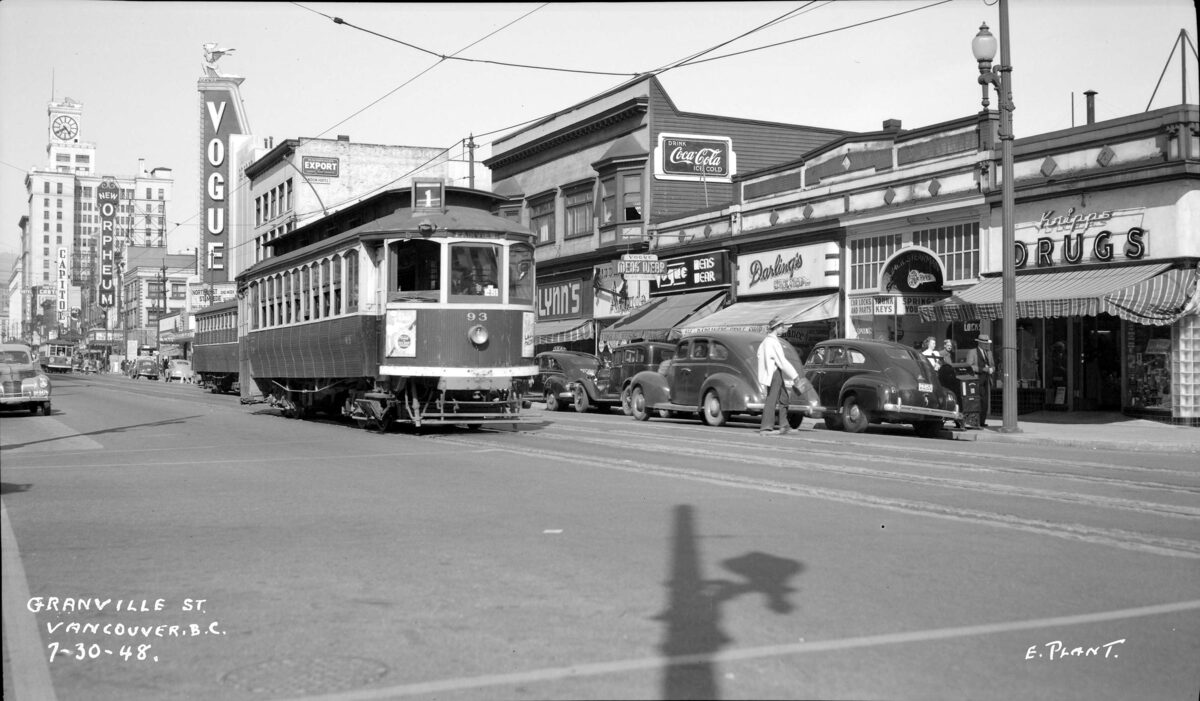 Granville Street in 1948 with streetcar, automobiles, and neon signs, Vancouver Block clock tower visible in background