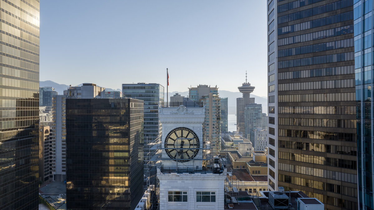 Aerial drone view of the clock tower nestled among modern skyscrapers with harbour and mountains behind